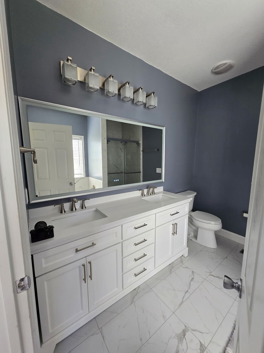Remodeled bathroom with white double vanity, framed mirror, and marble-look tile floor